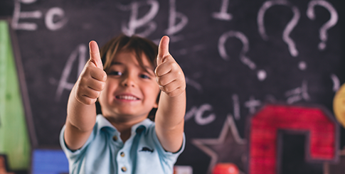 Kid with thumbs up and chalk board behind him.