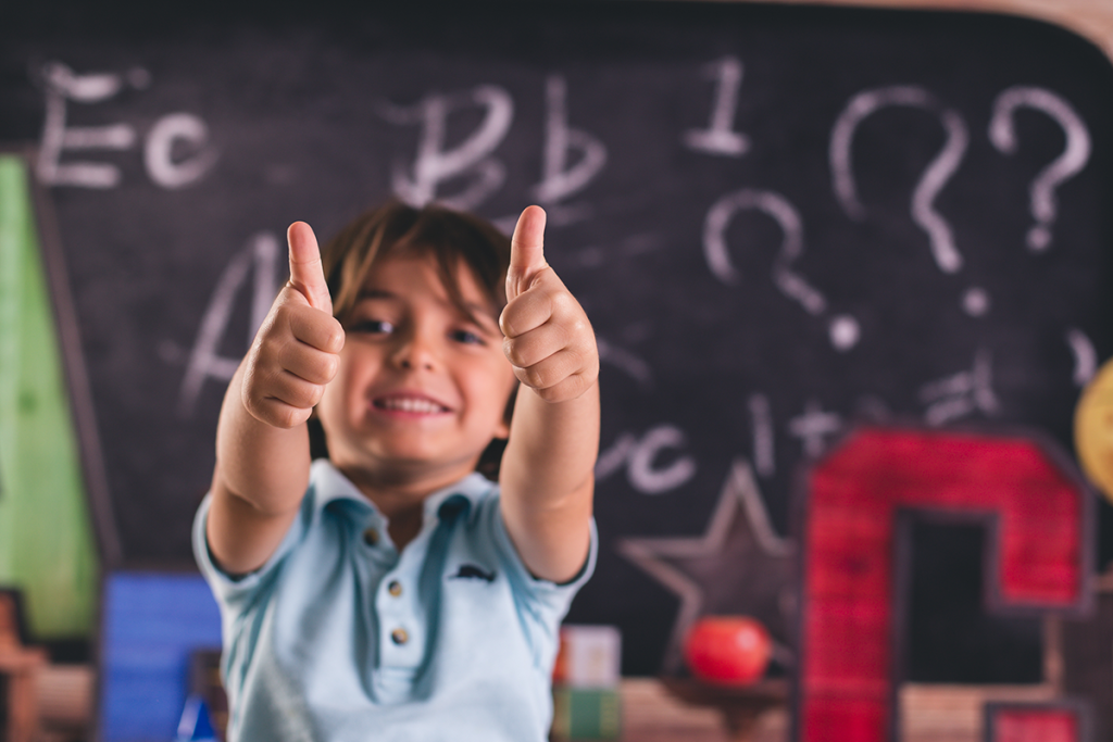 Kid with thumbs up and chalk board behind him.